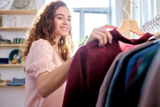 A woman standing next to a clothing rack and holding a blouse.