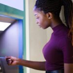 Young Black woman using a debit card at an ATM to withdraw money