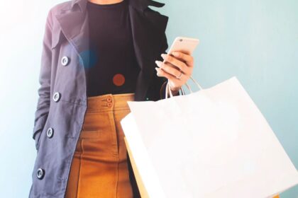 A woman holding a cell phone and bags in her hands as she shops.