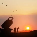 Artillery rocket system aimed to the sky and soldiers at sunset.