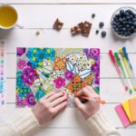 Overhead view of a woman using colored pencils to color a design in an adult coloring book.