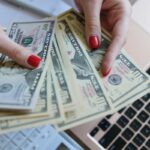 Closeup image of a woman's hands counting cash while using a laptop.