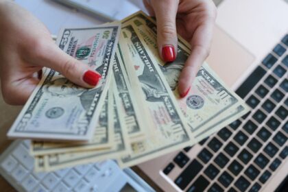 Closeup image of a woman's hands counting cash while using a laptop.