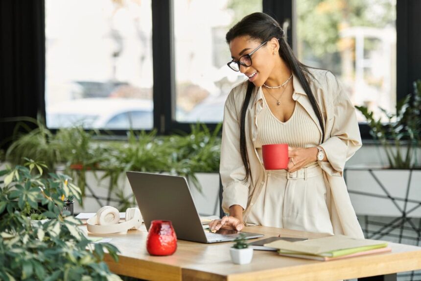 A woman working from her home office, holding a coffee mug while using her laptop.