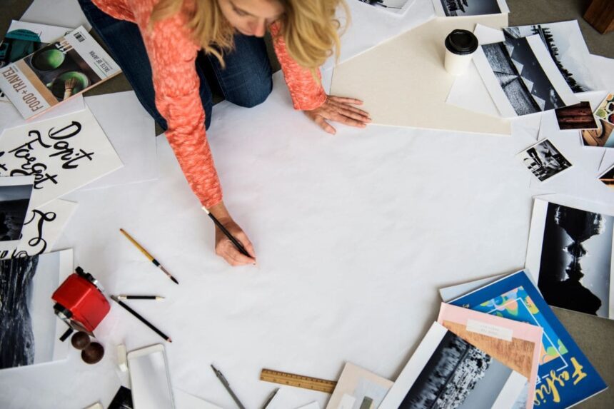 A woman working on a vision board on the floor, drawing on a large posterboard, with magazine cuttings and collage items in the background.
