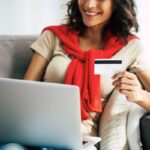 A woman sitting at home on a coach, using a laptop and holding a free Target giftcard.
