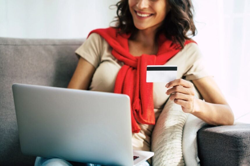 A woman sitting at home on a coach, using a laptop and holding a free Target giftcard.