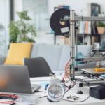 A home office desk, with a laptop, 3D printer, and other fabricating tools.