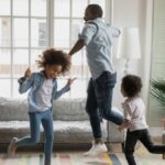 Black father and two young daughters dancing at home
