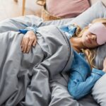 A woman sleeping in bed and wearing a sleep mask.
