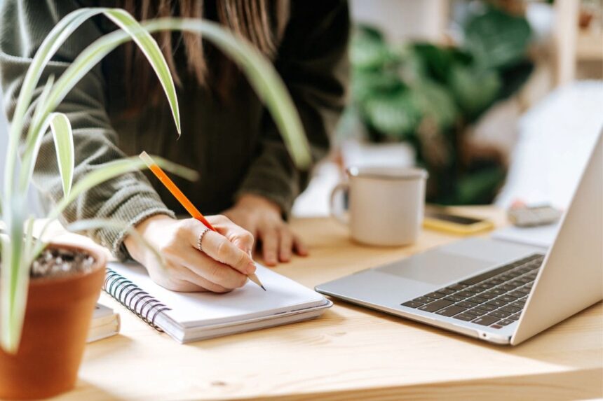 A woman working from home at a desk, surrounded by plants.