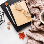 A business woman's home office desk, with a scarf, candle, notebooks, and fall leaves.