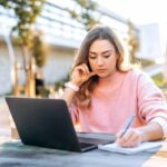 A woman working remotely from a cafe on a laptop outside.