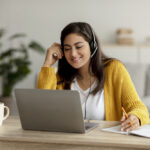 A woman wearing a sweater and headset working her Alorica work from home job