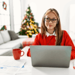 Young woman with long hair sitting at desk working on computer with Christmas free in the background