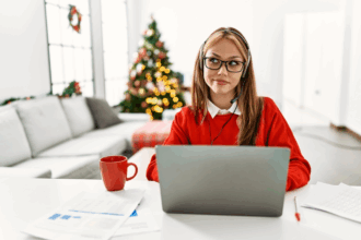 Young woman with long hair sitting at desk working on computer with Christmas free in the background
