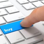 Finger clicking a button marked 'Buy' on a keyboard