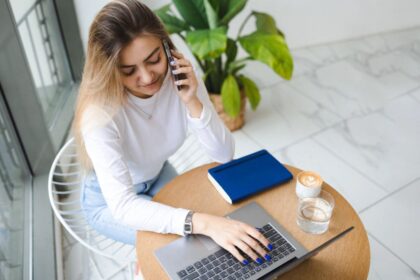 A young woman is working remotely in a cafe on a laptop and talking on the phone.