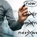 Man writing 'now' having crossed out 'later', 'tomorrow' and 'next week'