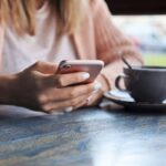 A woman sitting in a cafe, using a smartphone and drinking coffee.