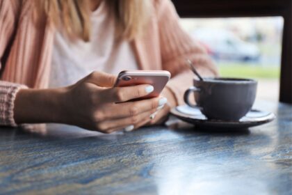 A woman sitting in a cafe, using a smartphone and drinking coffee.