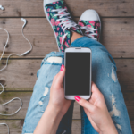 Young woman in ripped jeans and high top tennis shoes using a mobile phone