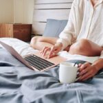 A woman working from home, using her laptop in bed while wearing pajamas.