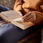A woman sitting on a couch, reading a book.