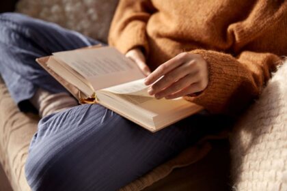 A woman sitting on a couch, reading a book.