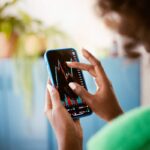 Black woman using smartphone at home, watching stock charts.