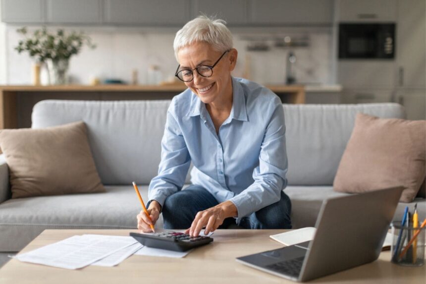 A woman working from home on her couch, using a laptop and calculator.