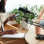 A woman recording a podcast, using a microphone and writing notes on a notepad.