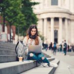 Female student sitting at the steps and using laptop