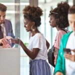 Smiling black woman showing e-ticket on smartphone to white male attendant at airport