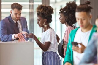 Smiling black woman showing e-ticket on smartphone to white male attendant at airport